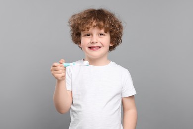 Photo of Cute little boy holding plastic toothbrush with paste on light grey background