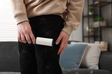 Pet shedding. Man with lint roller removing dog's hair from pants at home, closeup