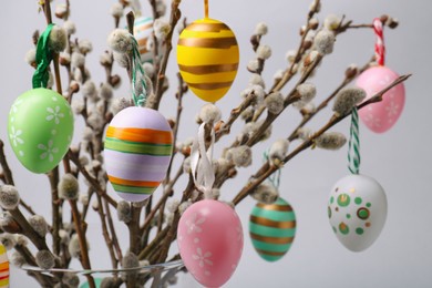 Photo of Vase with beautiful willow branches and painted Easter eggs on light grey background, closeup