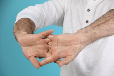 Photo of Man cracking his knuckles on light blue background, closeup. Bad habit