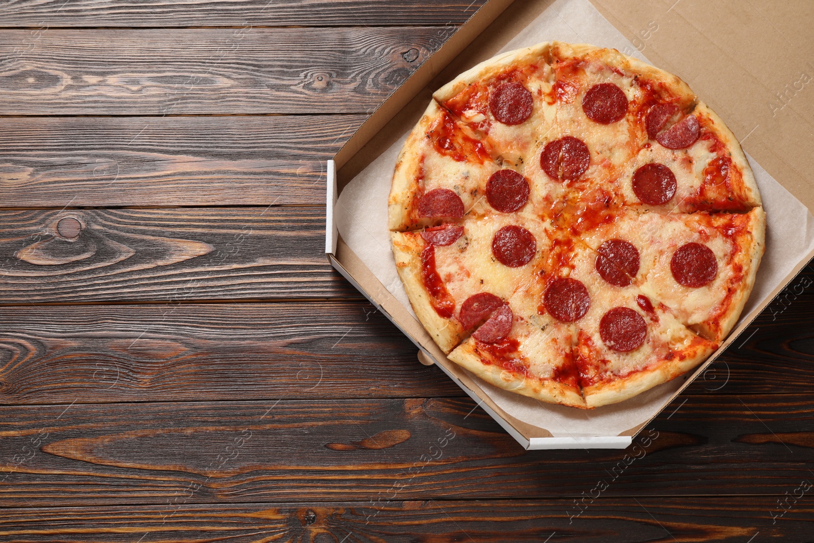 Photo of Hot delicious pepperoni pizza in cardboard box on wooden table, top view. Space for text