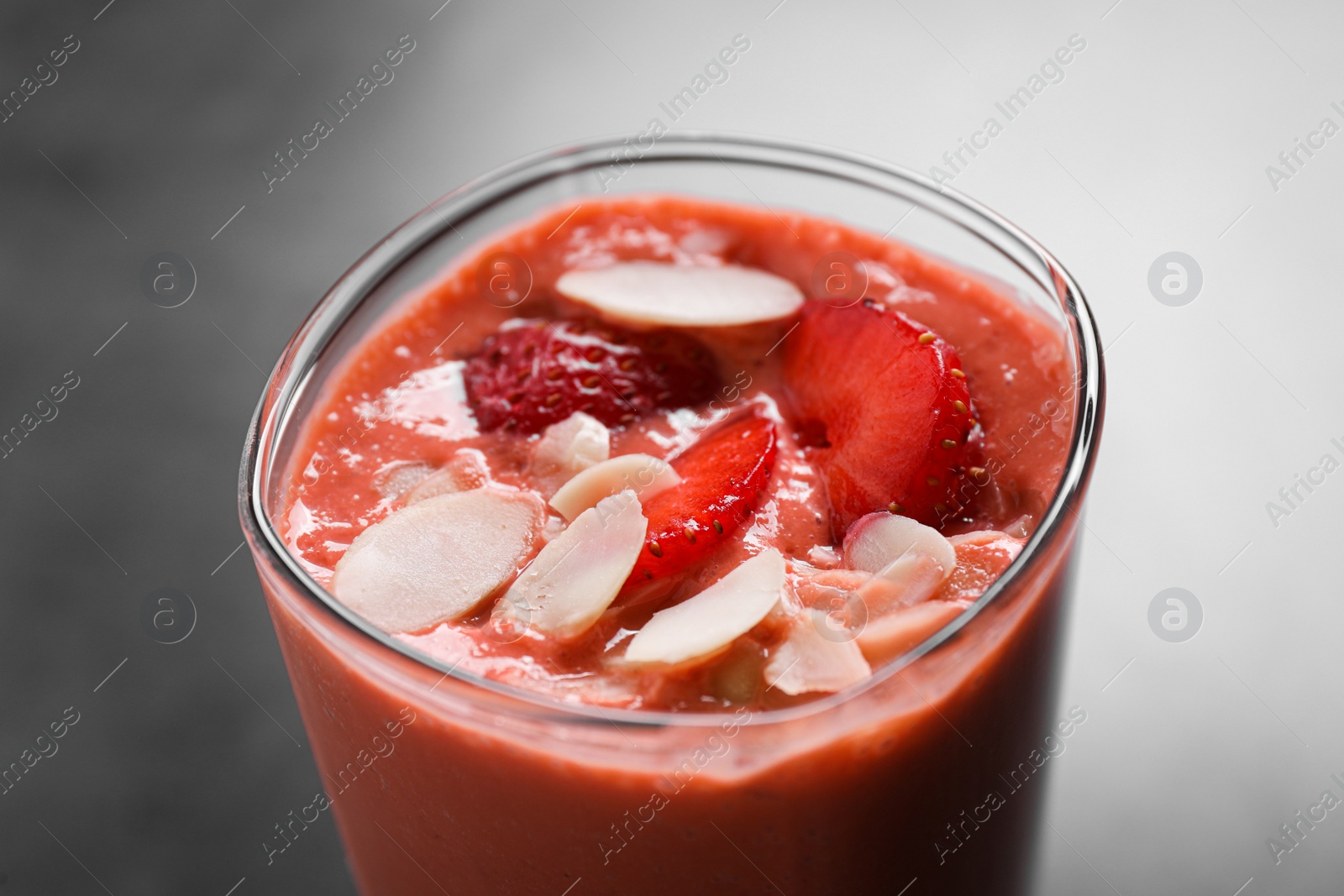 Photo of Glass of delicious smoothie with strawberry and almond flakes on grey table, closeup