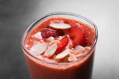 Photo of Glass of delicious smoothie with strawberry and almond flakes on grey table, closeup