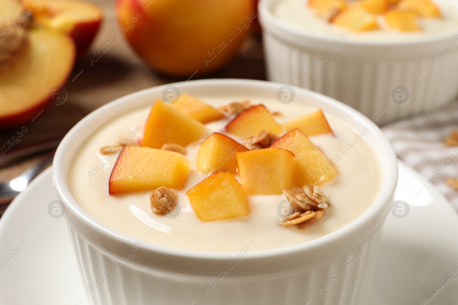 Photo of Tasty peach yogurt with granola and pieces of fruit in bowl on plate, closeup