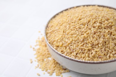 Photo of Raw bulgur in bowl on white table, closeup. Space for text
