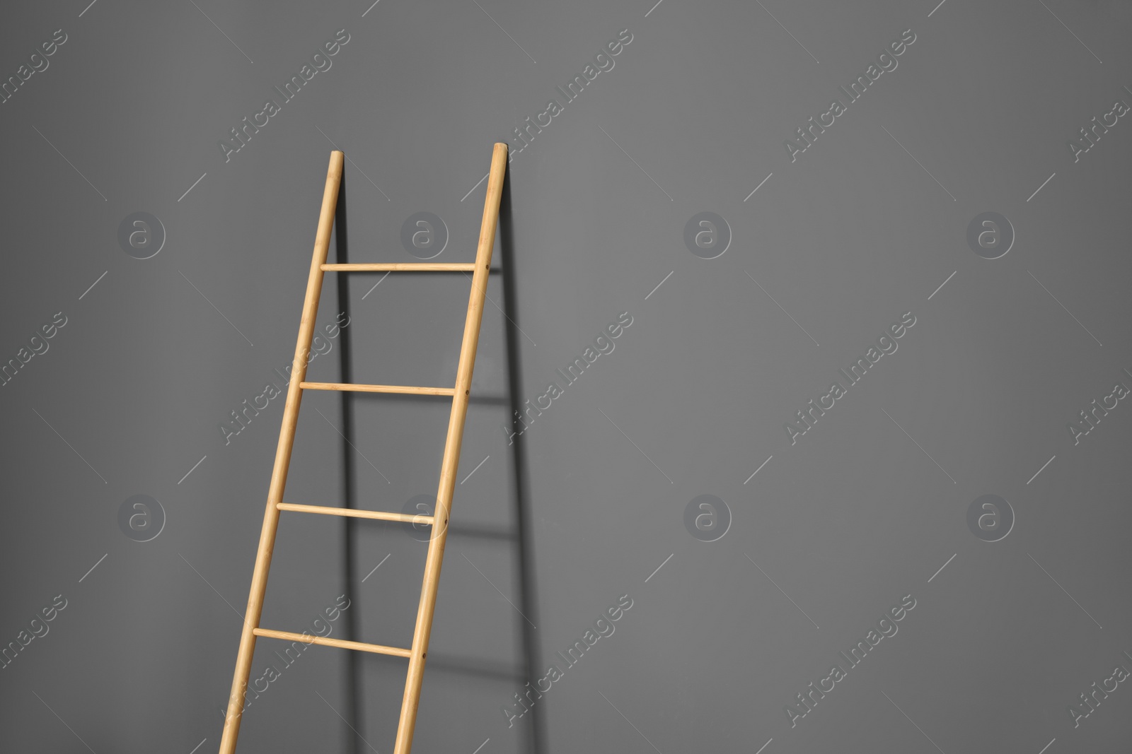 Photo of Modern wooden ladder on grey background. Space for text