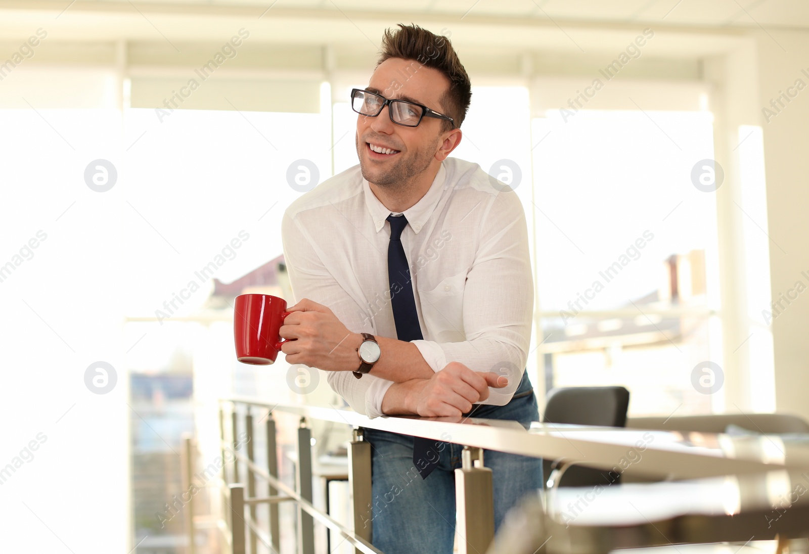 Photo of Young businessman with cup of drink relaxing in office during break