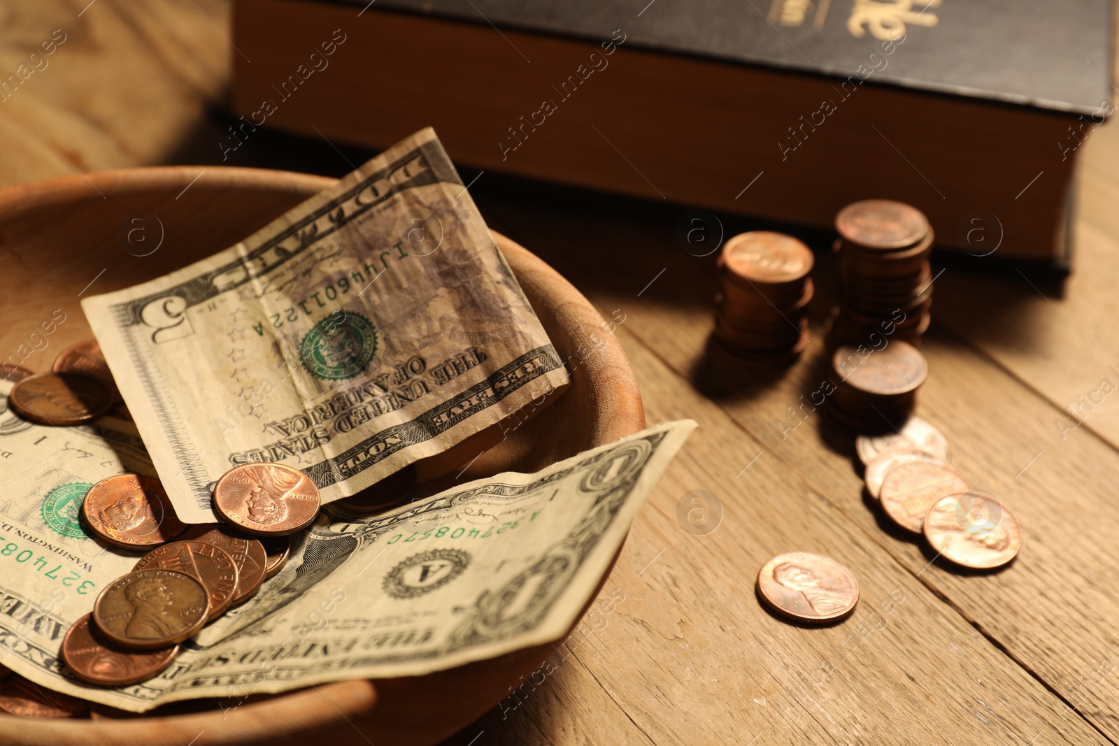 Photo of Donate and give concept. Bowl with coins, dollar banknotes and Bible on wooden table, closeup