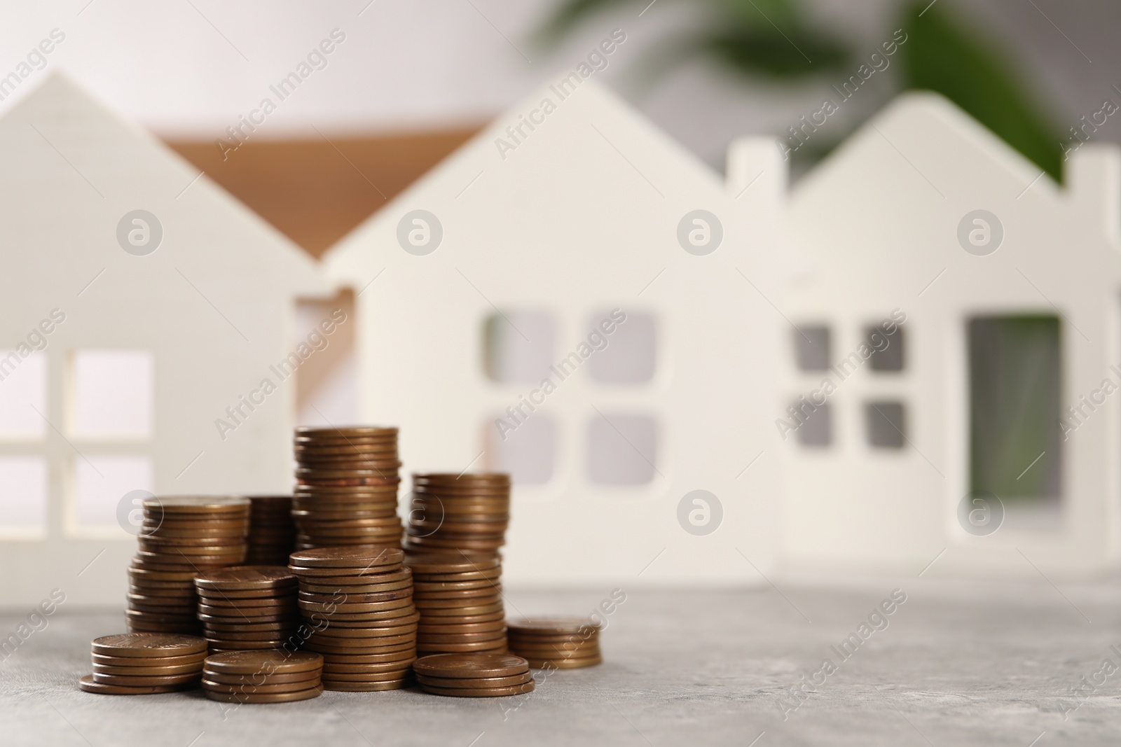 Photo of House models and stacked coins on grey table, selective focus. Space for text