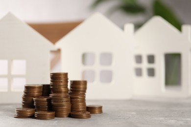 House models and stacked coins on grey table, selective focus. Space for text