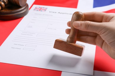 Photo of Immigration to United Kingdom. Woman stamping visa application form on flag, closeup
