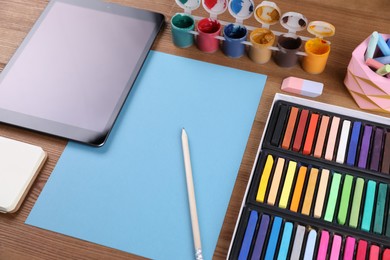 Photo of Blank sheet of paper, colorful chalk pastels, tablet and other drawing tools on wooden table. Modern artist's workplace
