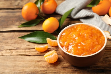 Photo of Tasty tangerine jam in bowl on wooden table. Space for text