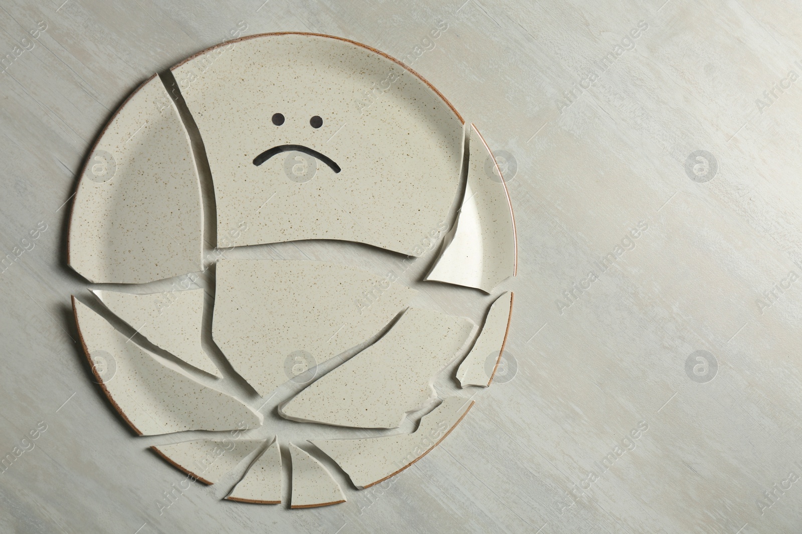 Photo of Broken plate with drawn sad face on light background, flat lay. Space for text