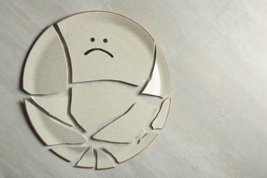 Photo of Broken plate with drawn sad face on light background, flat lay. Space for text
