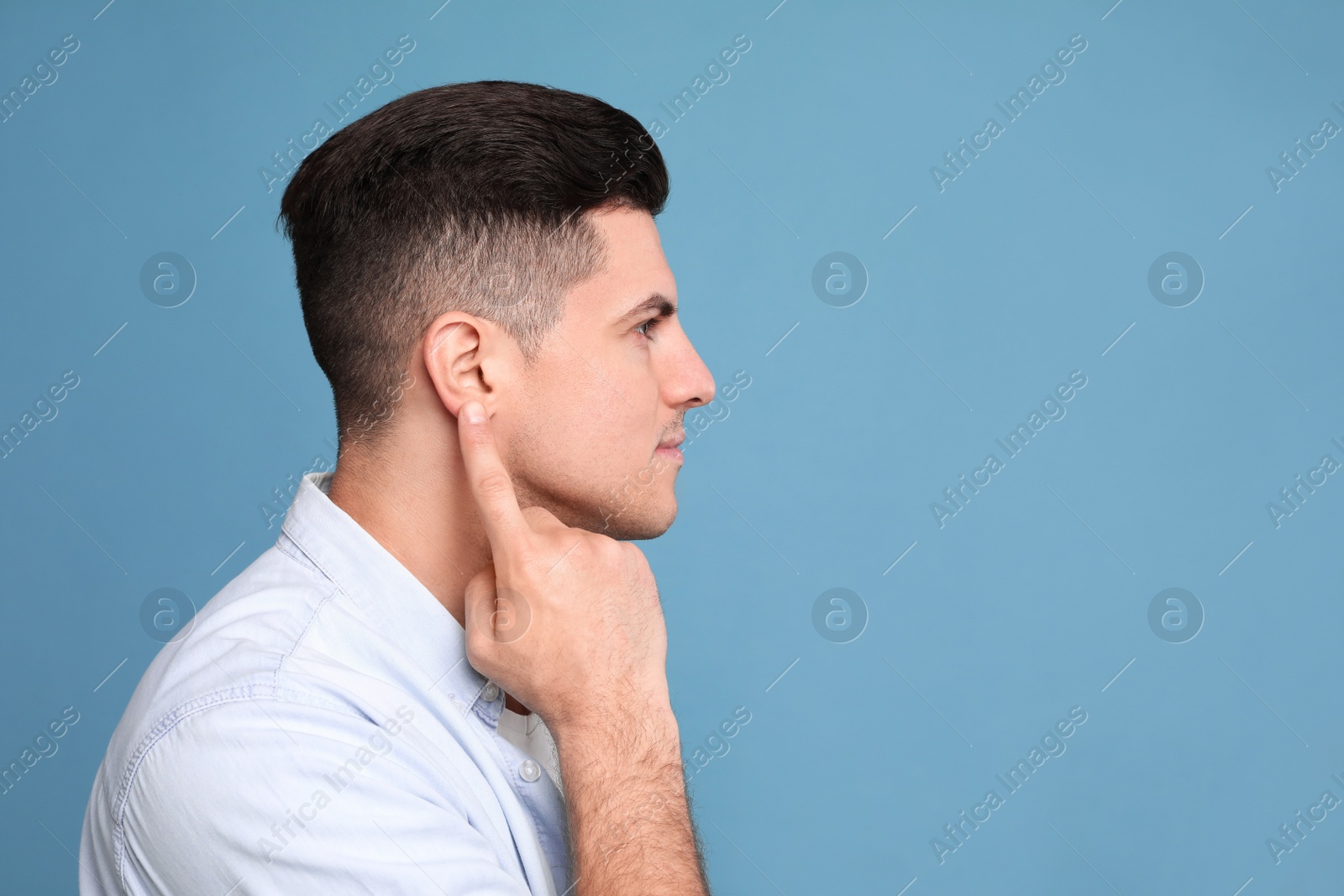 Photo of Man pointing at his ear on light blue background. Space for text