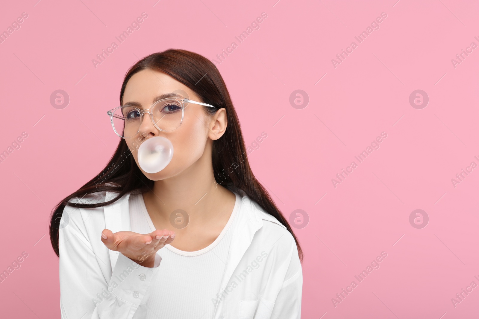 Photo of Beautiful woman blowing bubble gum on pink background, space for text