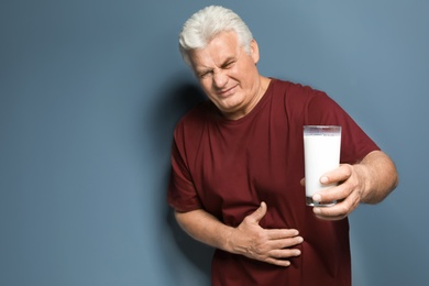 Photo of Mature man with dairy allergy holding glass of milk on color background