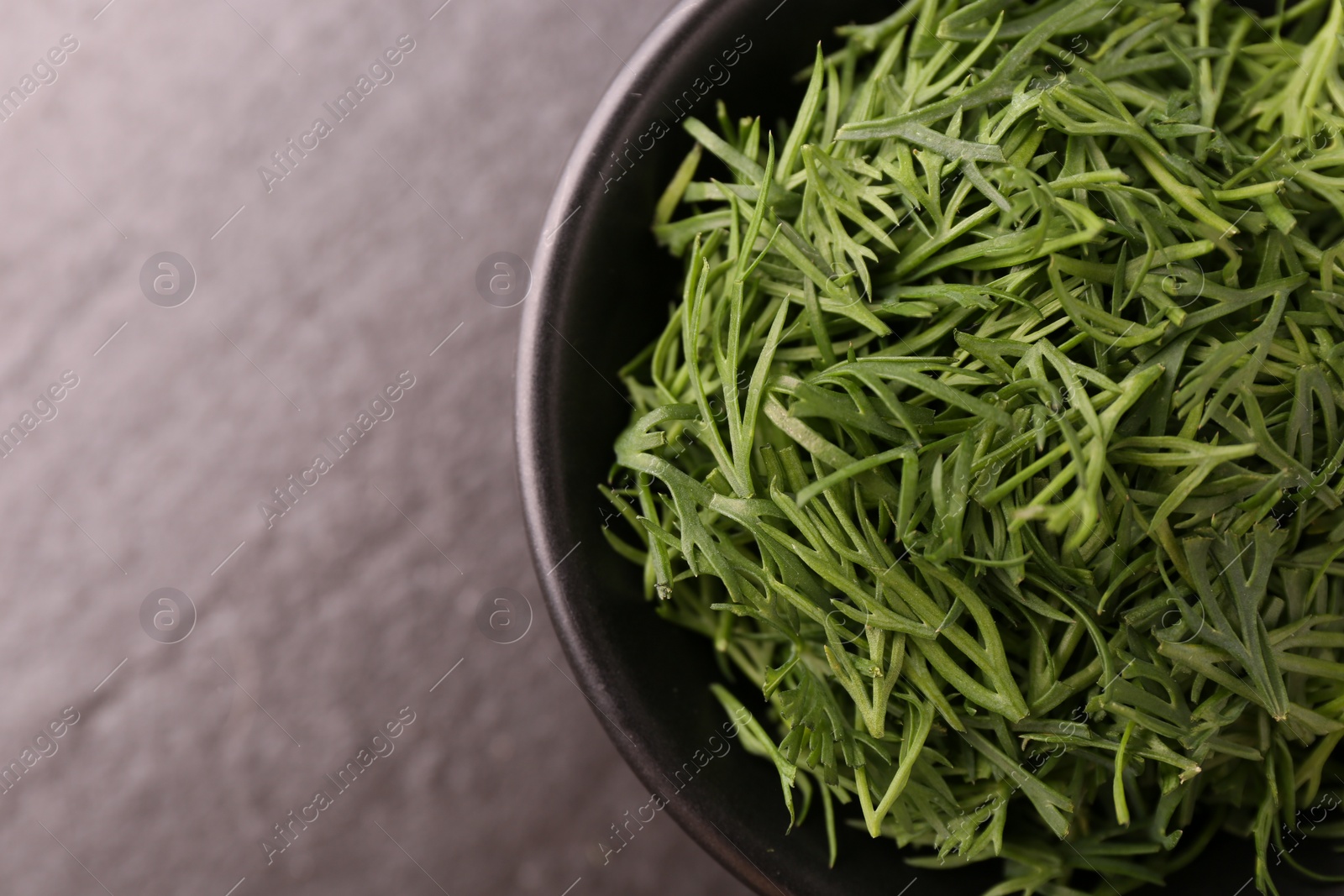 Photo of Fresh cut dill in bowl on dark table, top view. Space for text