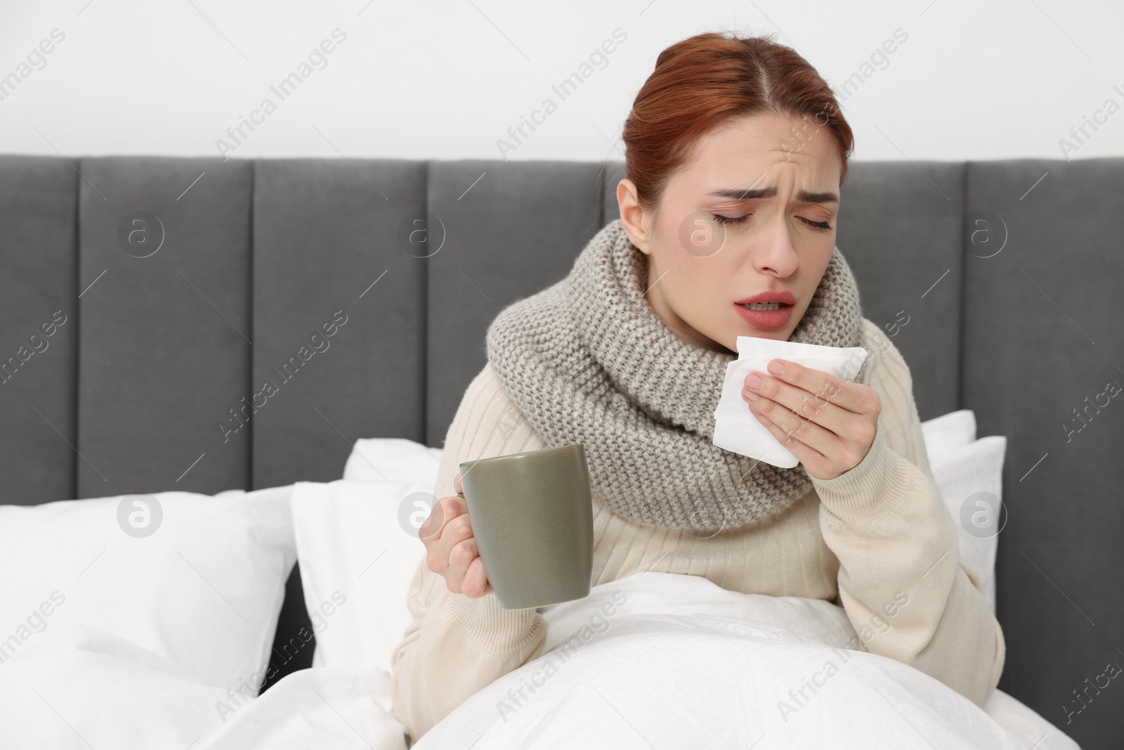 Photo of Woman with cup of drink and tissue coughing on bed, space for text. Cold symptoms