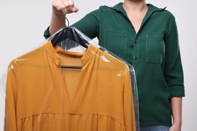 Photo of Dry-cleaning service. Woman holding dress in plastic bag on white background, closeup