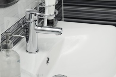 Photo of Clean white sink with shiny water tap in bathroom