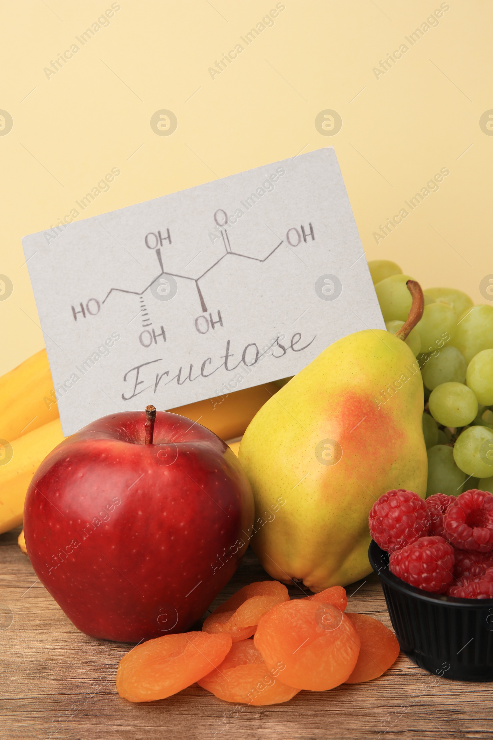 Photo of Card with word Fructose, delicious ripe fruits, raspberries and dried apricots on wooden table