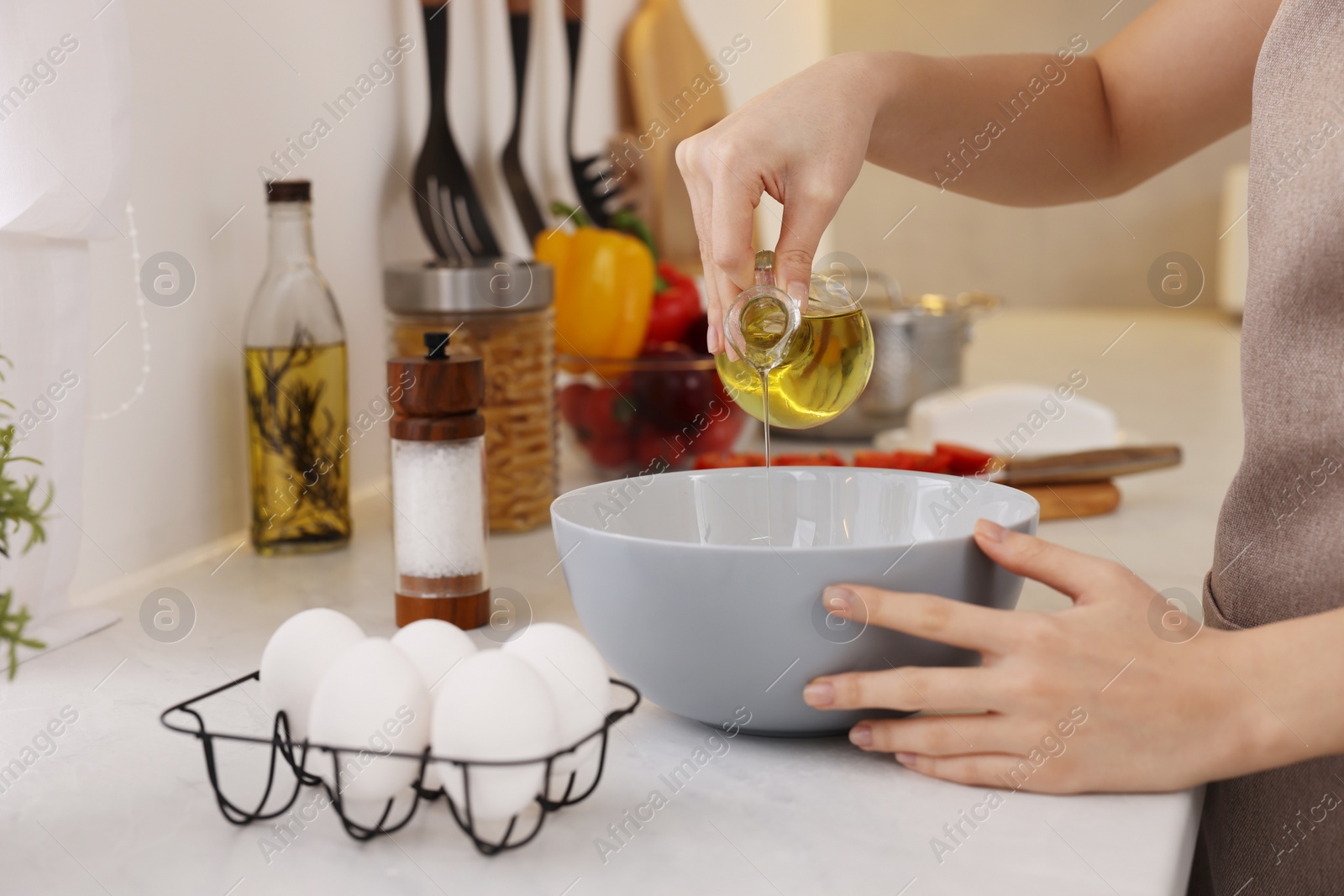 Photo of Cooking process. Woman pouring oil from bottle into bowl at light countertop indoors, closeup