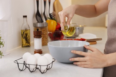 Cooking process. Woman pouring oil from bottle into bowl at light countertop indoors, closeup