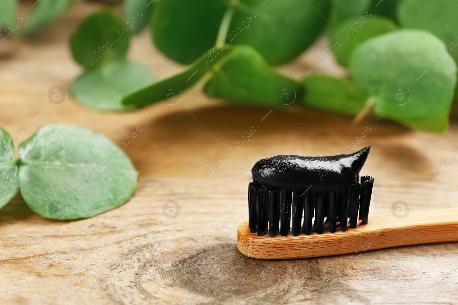 Photo of Bamboo toothbrush with charcoal paste on wooden  table, closeup. Space for text