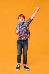 Photo of Cute schoolboy with backpack on orange background