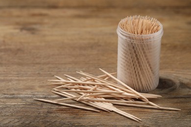 Photo of Disposable toothpicks and holder on wooden background. Space for text