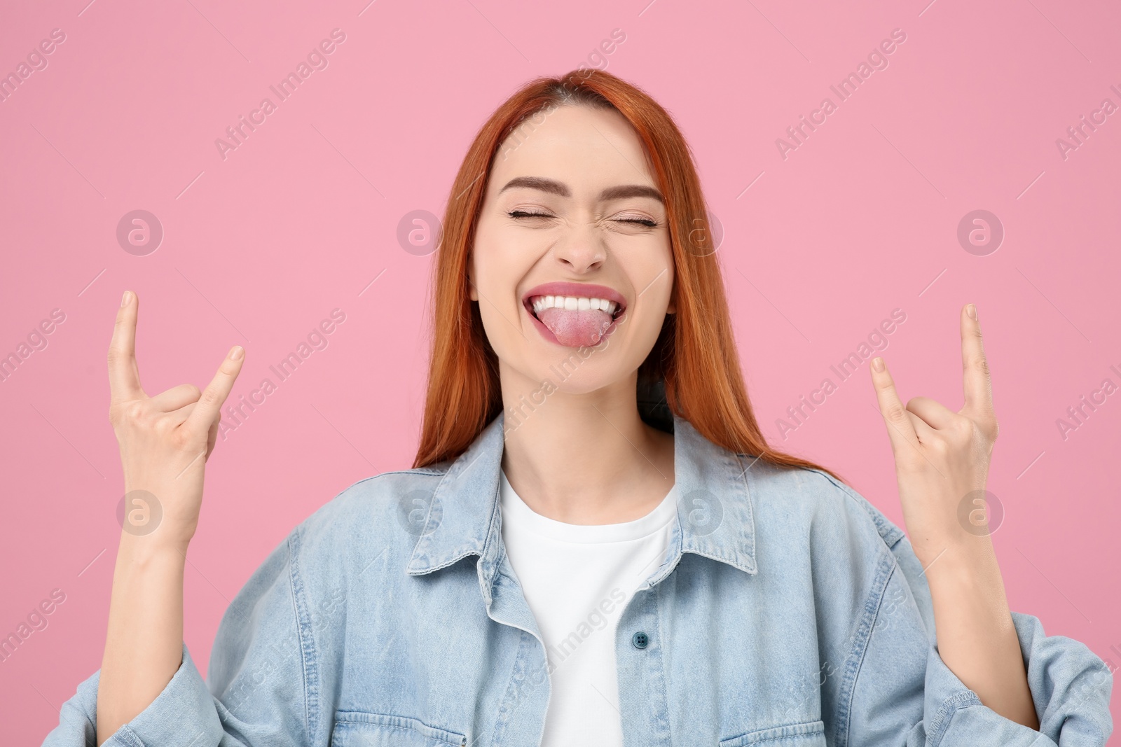 Photo of Happy woman showing her tongue and rock gesture on pink background