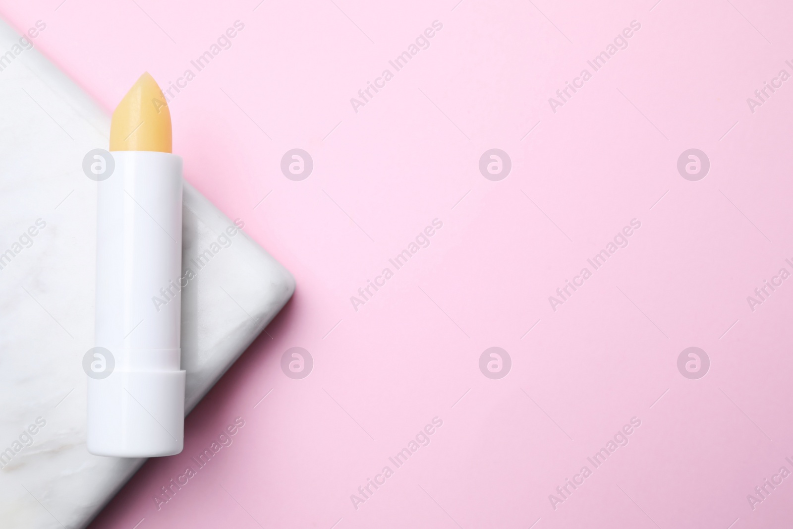 Photo of Hygienic lipstick and marble board on pink background, top view. Space for text