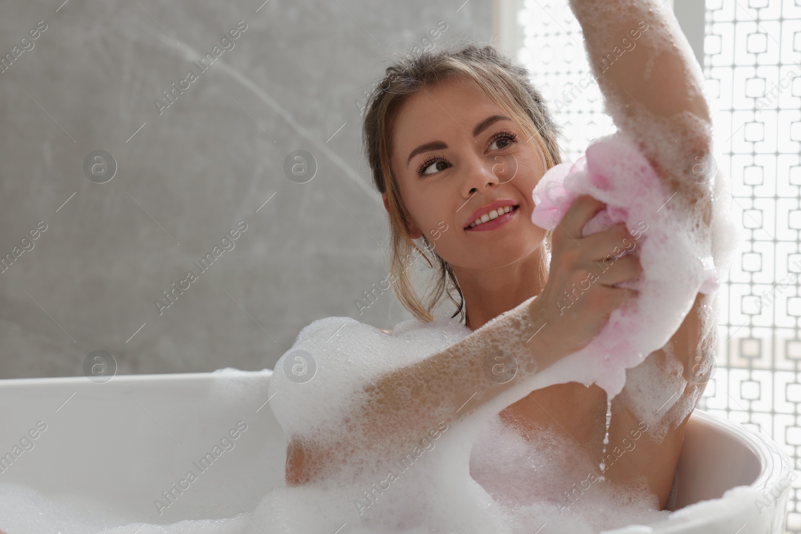 Photo of Beautiful woman with mesh pouf taking bath indoors, space for text