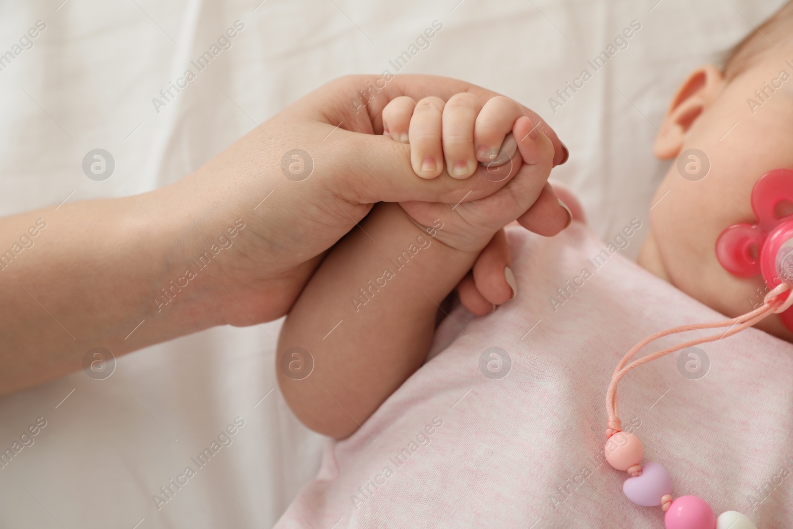 Photo of Mother holding baby's hand on bed, closeup