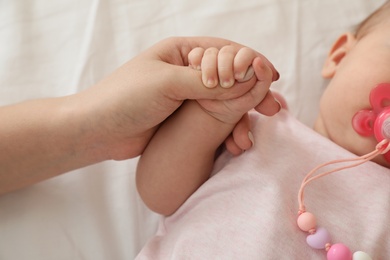 Mother holding baby's hand on bed, closeup