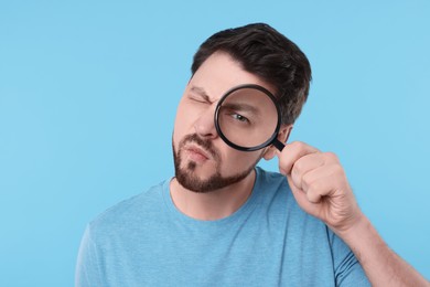 Photo of Confused man looking through magnifier glass on light blue background