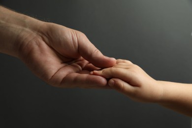 Photo of Father and child holding hands on dark grey background, closeup