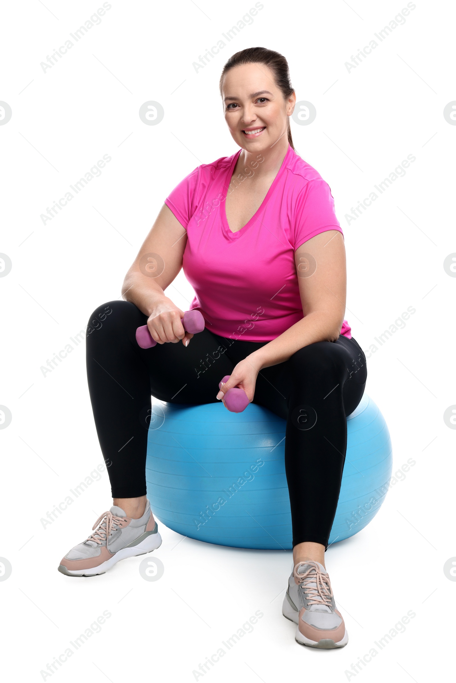 Photo of Happy overweight woman with dumbbells sitting on fitness ball against white background