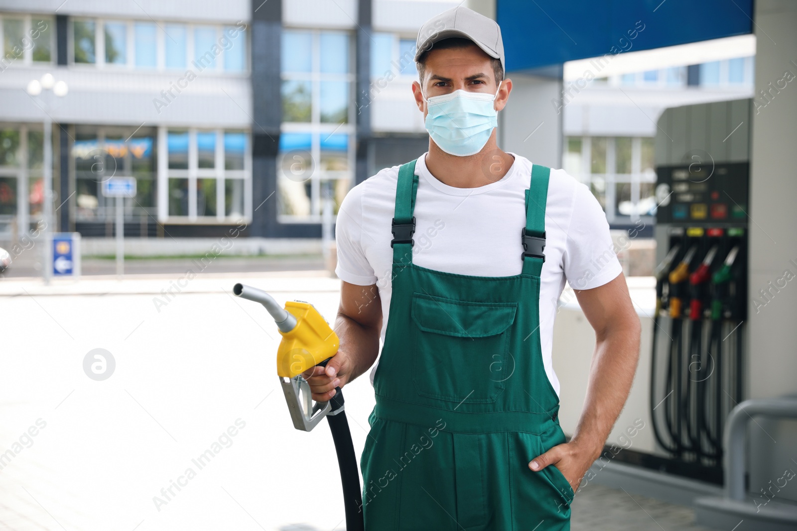 Photo of Worker in mask with fuel pump nozzle at modern gas station