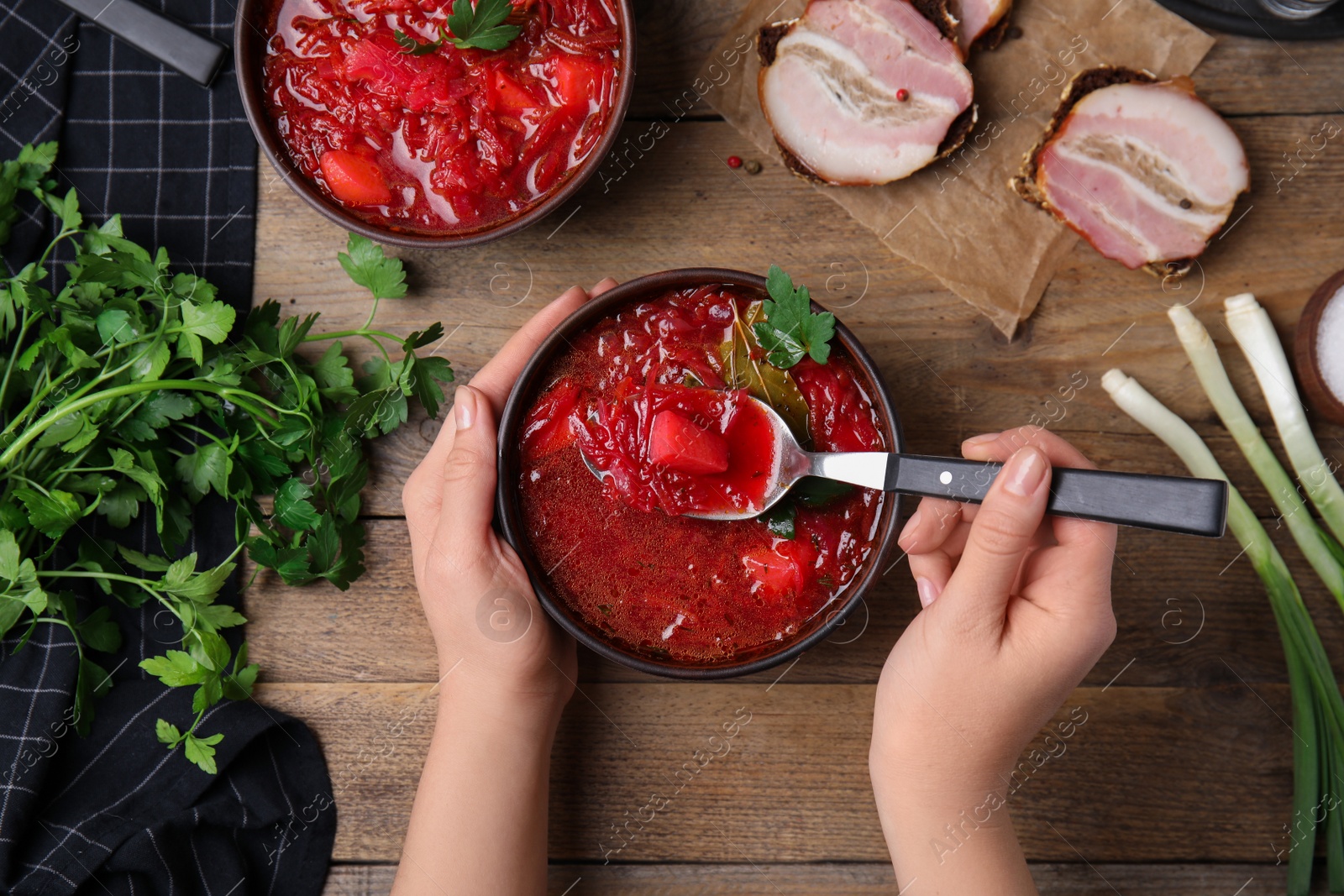 Photo of Woman with clay bowl of Ukrainian borsch at wooden table, top view