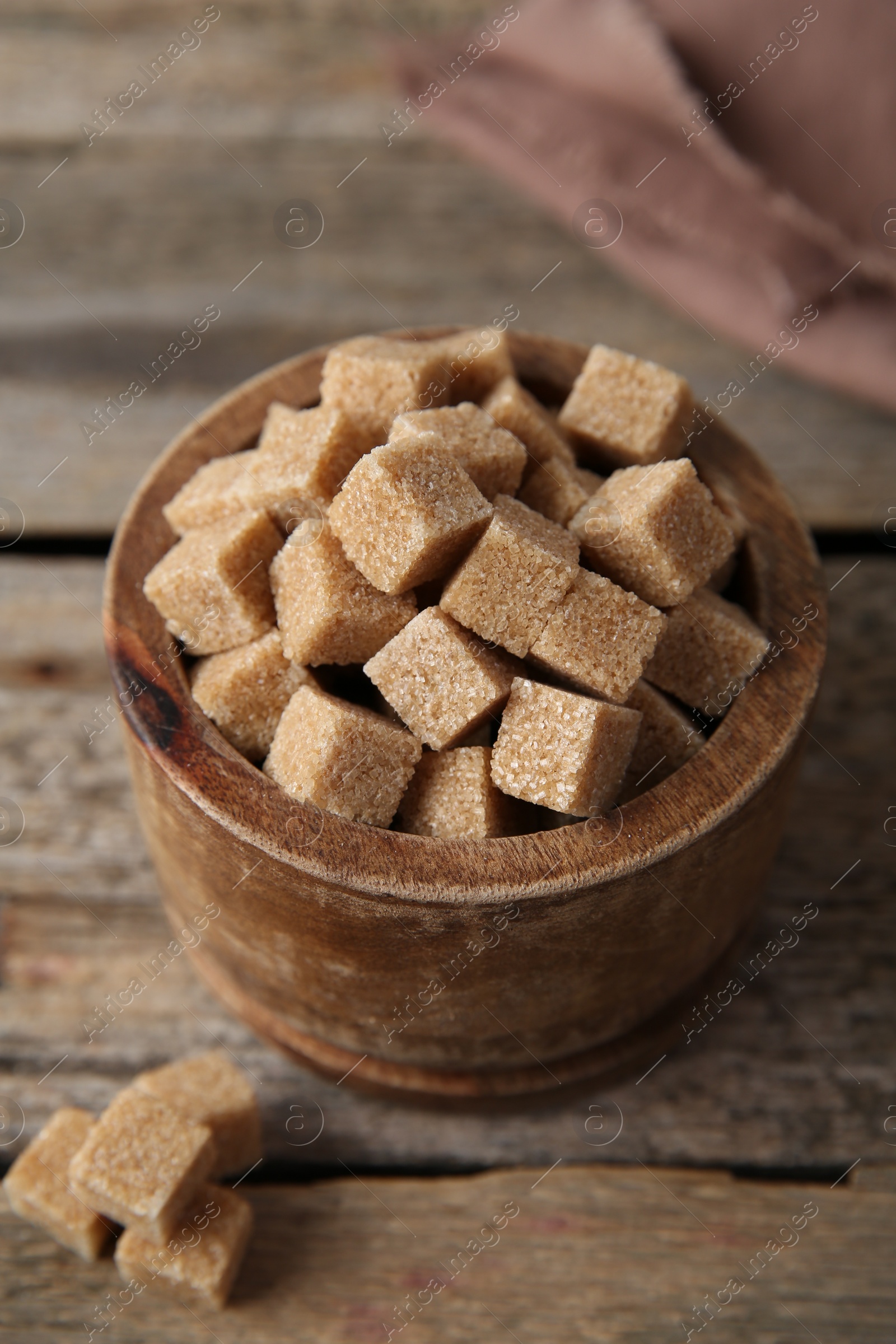 Photo of Brown sugar cubes in bowl on wooden table, closeup