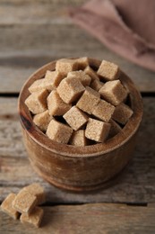 Photo of Brown sugar cubes in bowl on wooden table, closeup