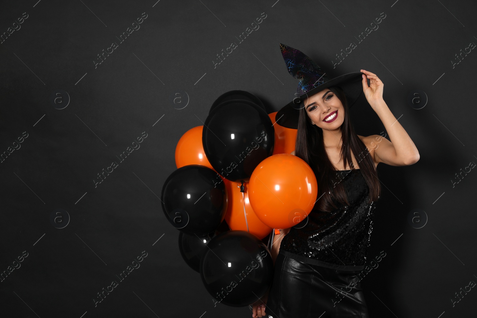 Photo of Beautiful woman wearing witch costume with balloons for Halloween party on black background