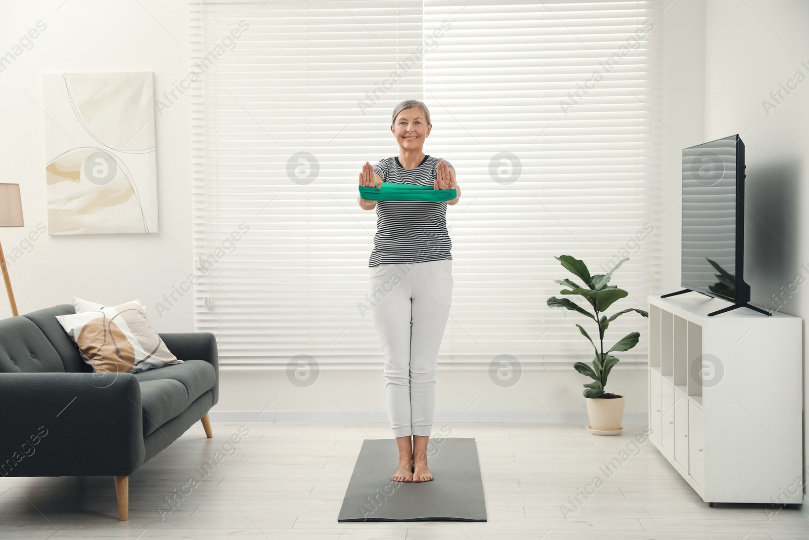 Photo of Senior woman doing exercise with fitness elastic band on mat at home