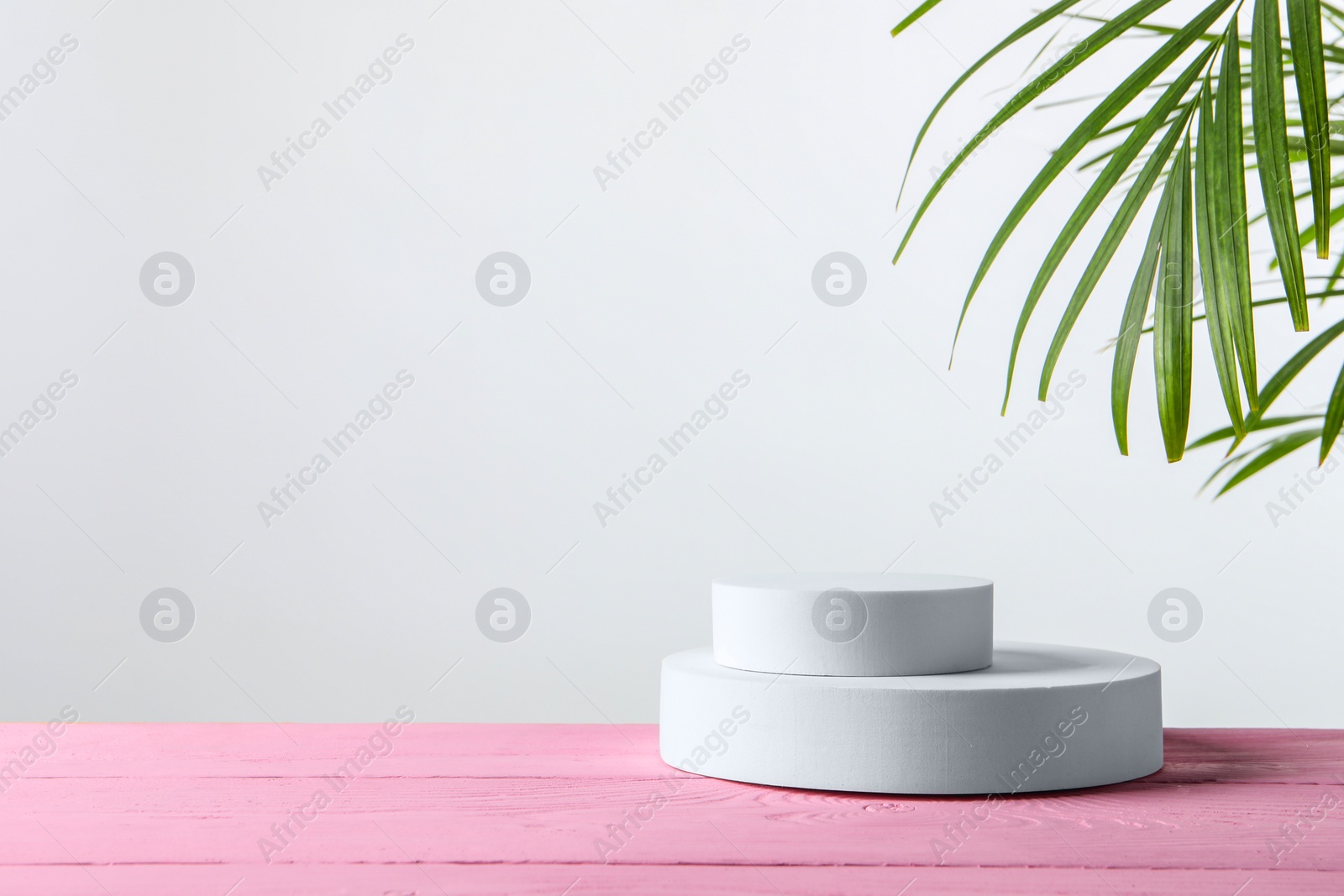 Photo of Green leaves and round shaped podium on pink wooden table. Space for text