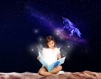 Cute little girl reading magic book. Night sky with stars and fairy unicorn on background 