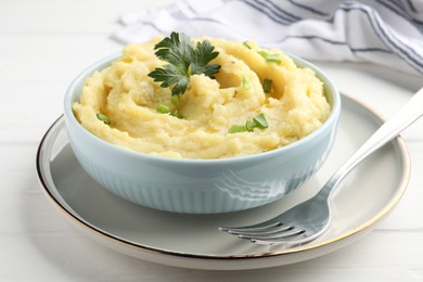 Photo of Bowl of tasty mashed potatoes with parsley and green onion served on white wooden table, closeup