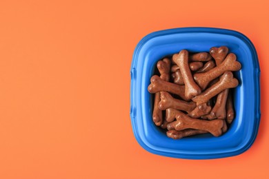 Blue bowl with bone shaped dog cookies on orange background, top view. Space for text